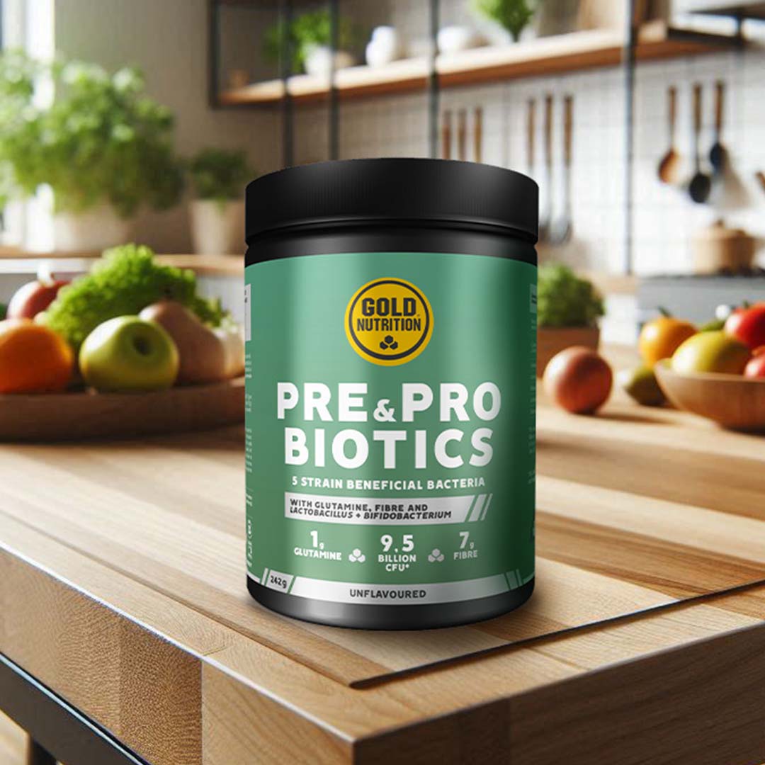 Bote de suplemento GoldNutrition que contiene Prebióticos y Probióticos, con 5 cepas de bacterias beneficiosas, glutamina, fibra y 9,5 mil millones de UFC. El producto está en una cocina con frutas y verduras al fondo | Pre&Pro Biotics