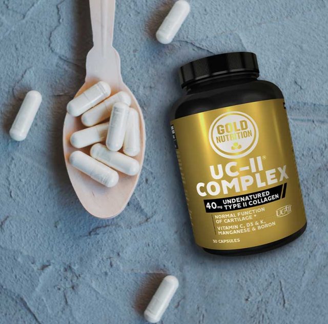 Fotografía de un frasco de suplemento alimenticio marca Gold Nutrition, llamado UC-II Complex, que contiene colágeno tipo II no desnaturalizado (40 mg por cápsula). El frasco es negro con una etiqueta dorada y negra, acompañado de una cuchara de madera con cápsulas blancas sobre una superficie azul texturizada. El producto menciona que apoya la función normal del cartílago e incluye vitaminas C, D3 y K, además de manganeso y boro. Contiene 30 cápsulas.